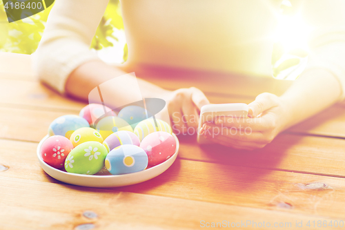 Image of close up of hands with easter eggs and smartphone