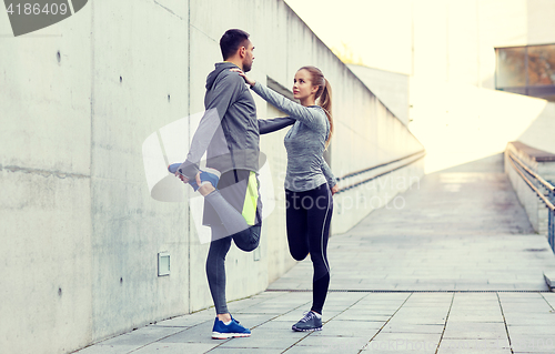 Image of smiling couple stretching leg outdoors