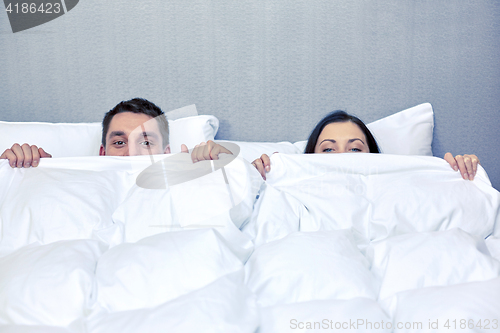 Image of happy couple hiding under blanket in bed