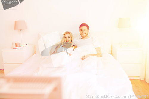 Image of happy couple lying in bed at home and watching tv