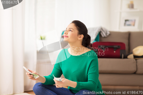 Image of happy woman with money and travel bag at home