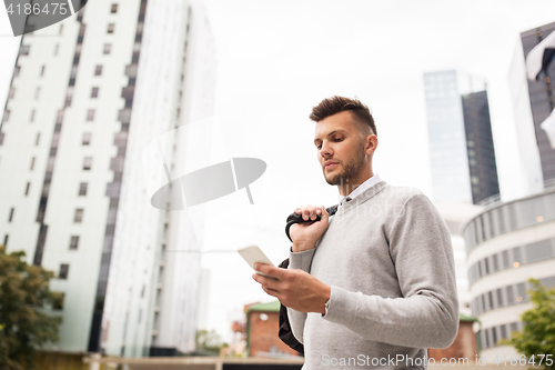 Image of young man with bag texting on smartphone in city