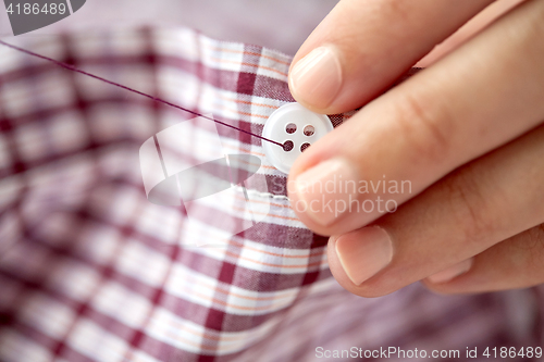 Image of woman with needle stitching on button to shirt