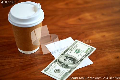 Image of coffee in paper cup, bill and money on table