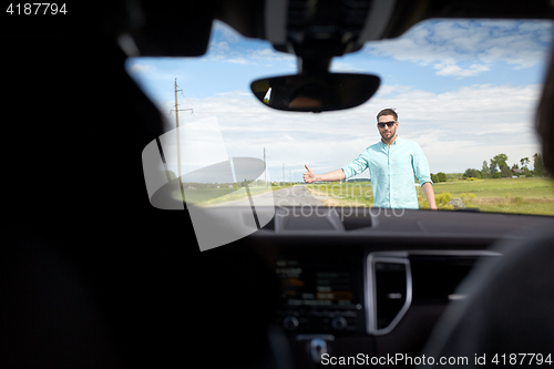 Image of man hitchhiking and stopping car with thumbs up