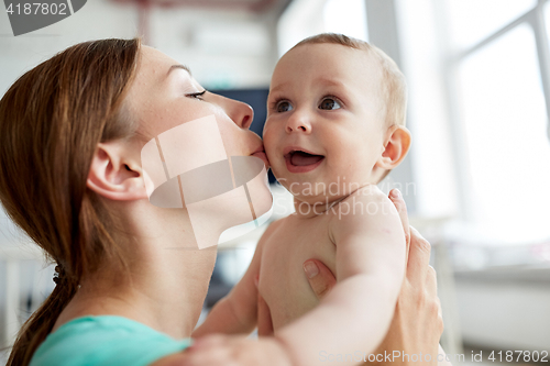 Image of happy young mother kissing little baby at home