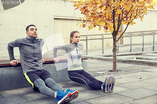 Image of couple doing triceps dip on city street bench