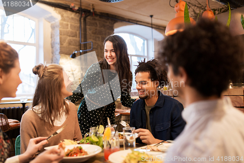 Image of happy friends eating and drinking at restaurant