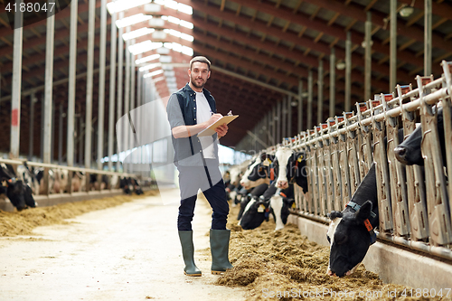 Image of farmer with clipboard and cows in cowshed on farm