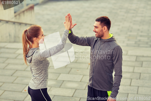 Image of happy couple giving high five outdoors