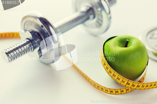 Image of close up of dumbbell and apple with measuring tape