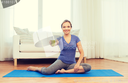 Image of happy woman with smoothie sitting on mat at home
