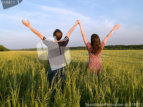 Image of Young Couple in Field Holding Hands Up