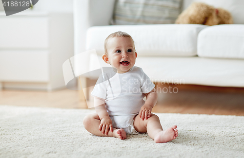 Image of happy baby boy or girl sitting on floor at home