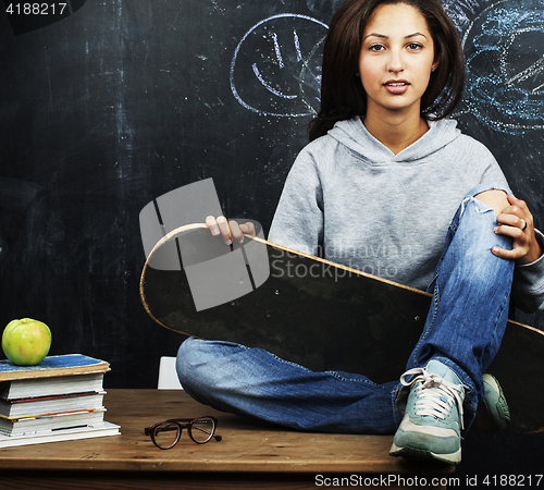 Image of young cute teenage girl in classroom at blackboard seating on ta
