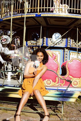 Image of cool real teenage girl with candy near carousels at amusement pa