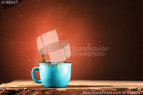 Image of Brown splashes out drink from cup of tea on a brown background