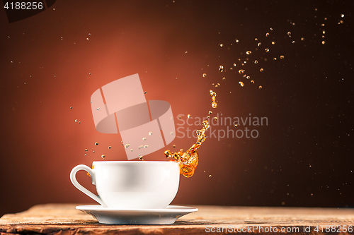 Image of Brown splashes out drink from cup of tea on a brown background