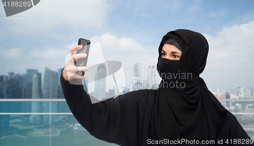 Image of muslim woman in hijab taking selfie by smartphone