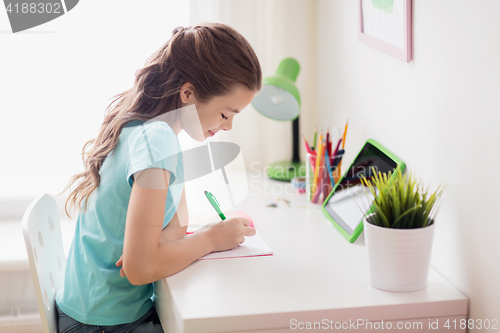 Image of girl with tablet pc writing to notebook at home