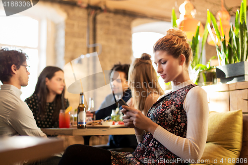 Image of woman with smartphone and friends at restaurant
