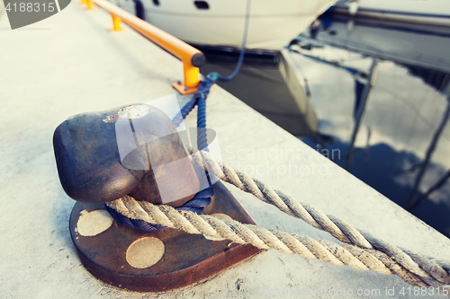 Image of rusted iron mooring bollard with rope on pier