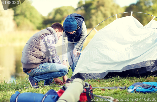 Image of happy father and son setting up tent outdoors