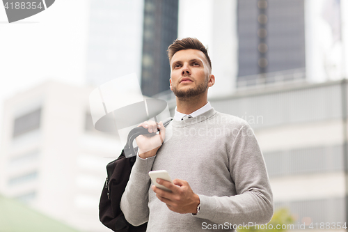 Image of young man with smartphone and bag in city