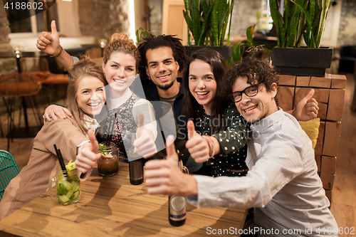 Image of happy friends with drinks showing thumbs up at bar