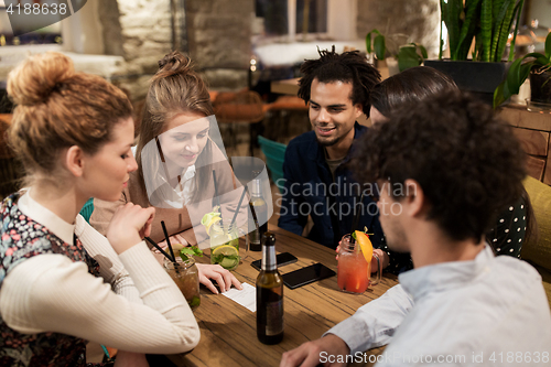 Image of happy friends with drinks and bill at bar or cafe