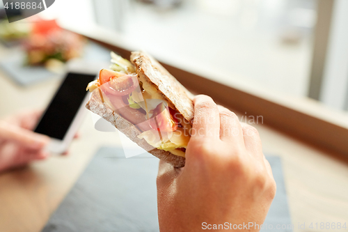 Image of hand with salmon panini sandwich at restaurant