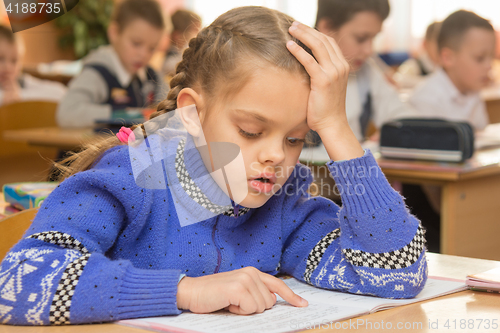 Image of First-grader at a lesson reads the text line by line leading a finger, in the background other students