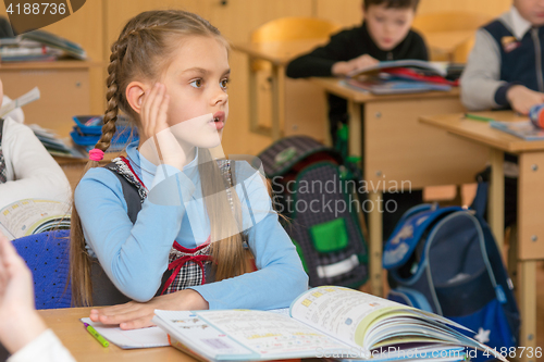 Image of Girl schoolgirl at a lesson at school answers the question after raising his hand