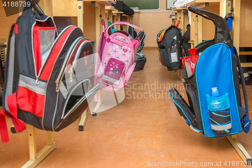 Image of School bags hanging on hangers on both sides of the aisle between the desks in the classroom