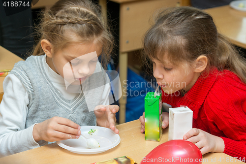 Image of Two children are drinking juice and eating cake at a party at school