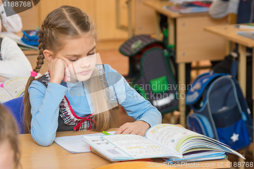 Image of A girl pupil in the classroom at school looking at a textbook