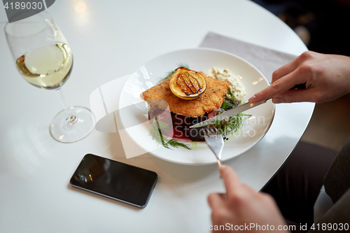 Image of woman with smartphone eating salad at restaurant