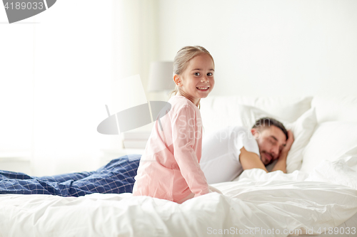 Image of little girl waking her sleeping father up in bed