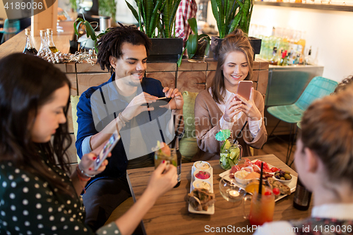 Image of friends with smartphones and food at restaurant