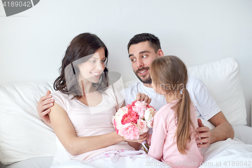 Image of happy girl giving flowers to mother in bed at home