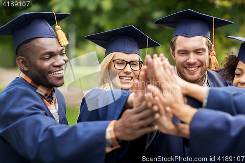 Image of happy students in mortar boards making high five