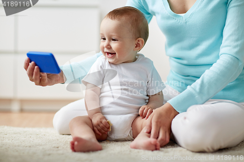 Image of happy mother showing smartphone to baby at home