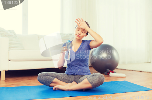 Image of tired woman drinking water after workout at home