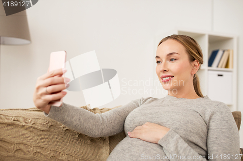 Image of pregnant woman taking smartphone selfie at home