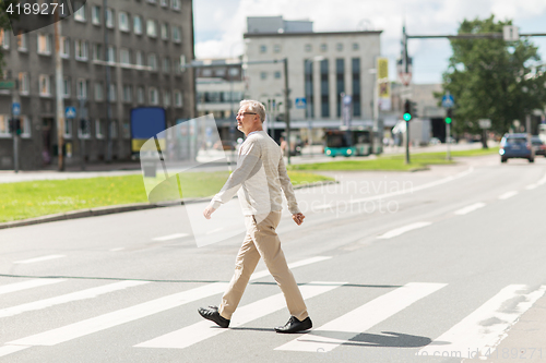 Image of senior man walking along city crosswalk