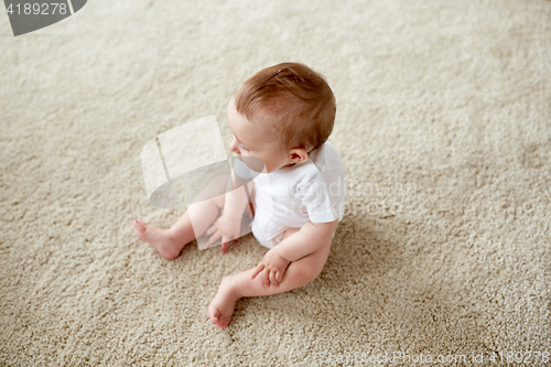 Image of happy baby boy or girl sitting on floor at home