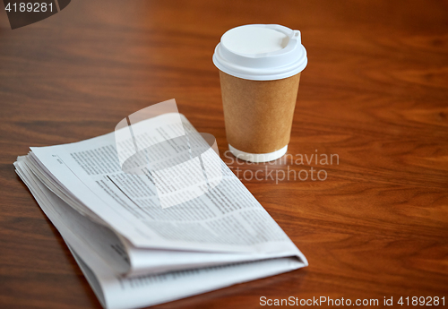 Image of coffee drink in paper cup and newspaper on table
