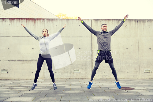 Image of happy man and woman jumping outdoors