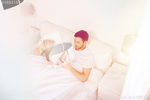 Image of man texting message while woman is sleeping in bed