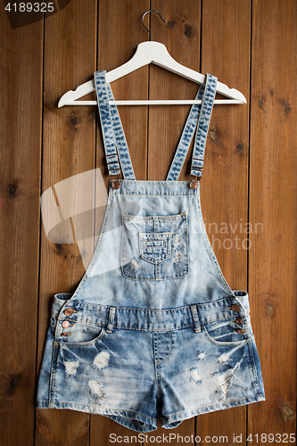 Image of denim or jeans overalls with hanger on wood